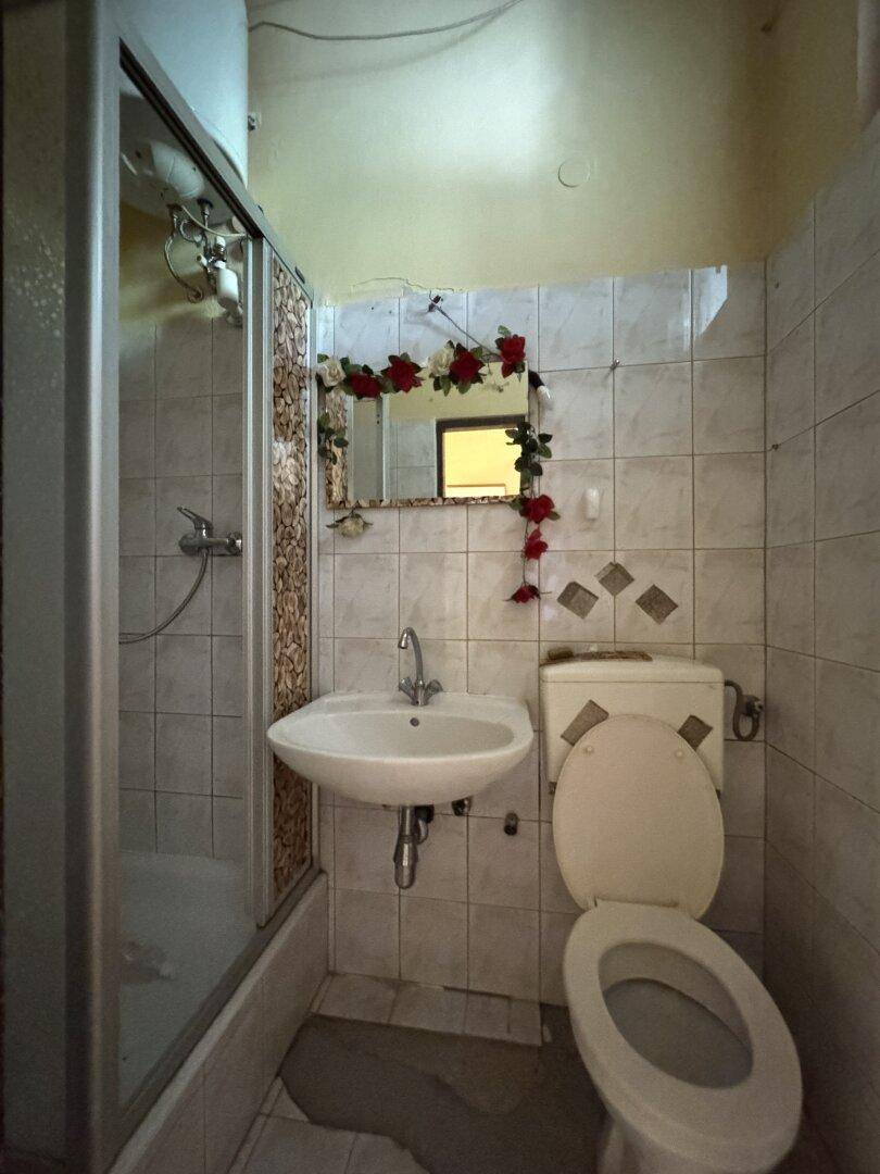 Kleines Badezimmer mit Duschkabine, WC und Waschbecken, ausgestattet mit hellen Fliesen.