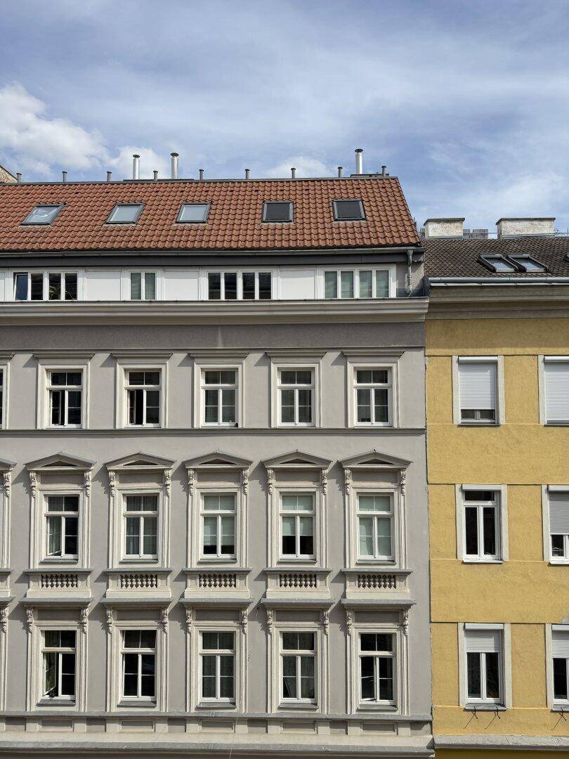 Historische Fassade eines Mehrfamilienhauses mit vielen Fenstern und rotem Ziegeldach.