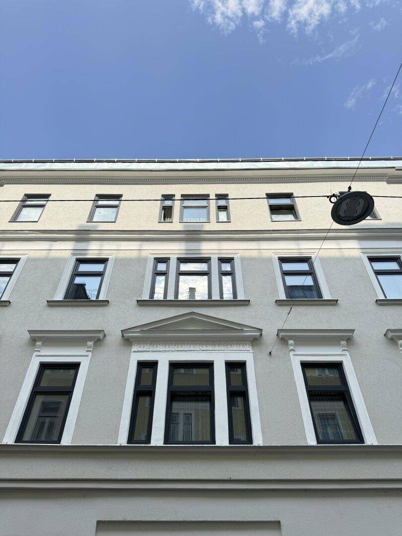 Fassade eines gepflegten Altbaus mit klassischen Fenstern und dekorativen Elementen unter blauem Himmel.
