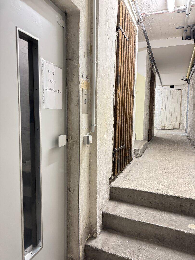 Kellerflur mit Lagerräumen und einem Aufzug, der zu den oberen Etagen führt.