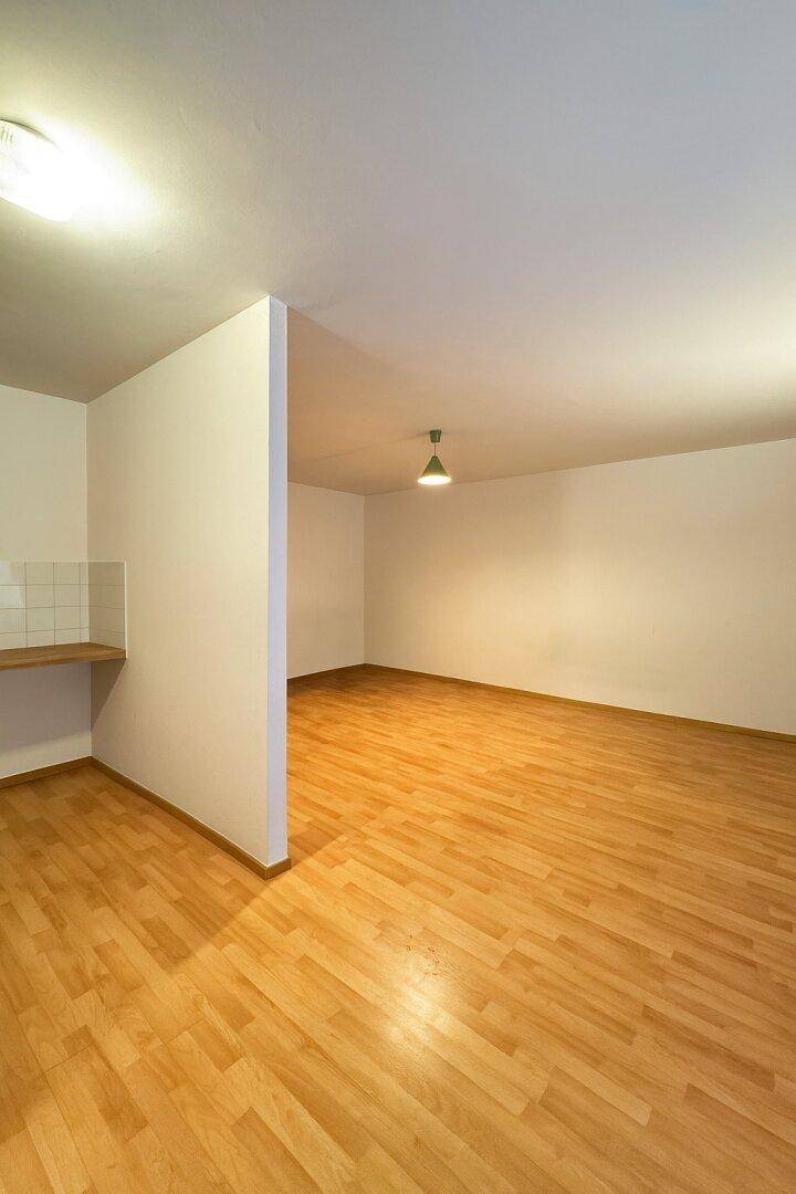 Geräumiger, leerer Raum mit Parkettboden und einer kleinen gefliesten Wandfläche.