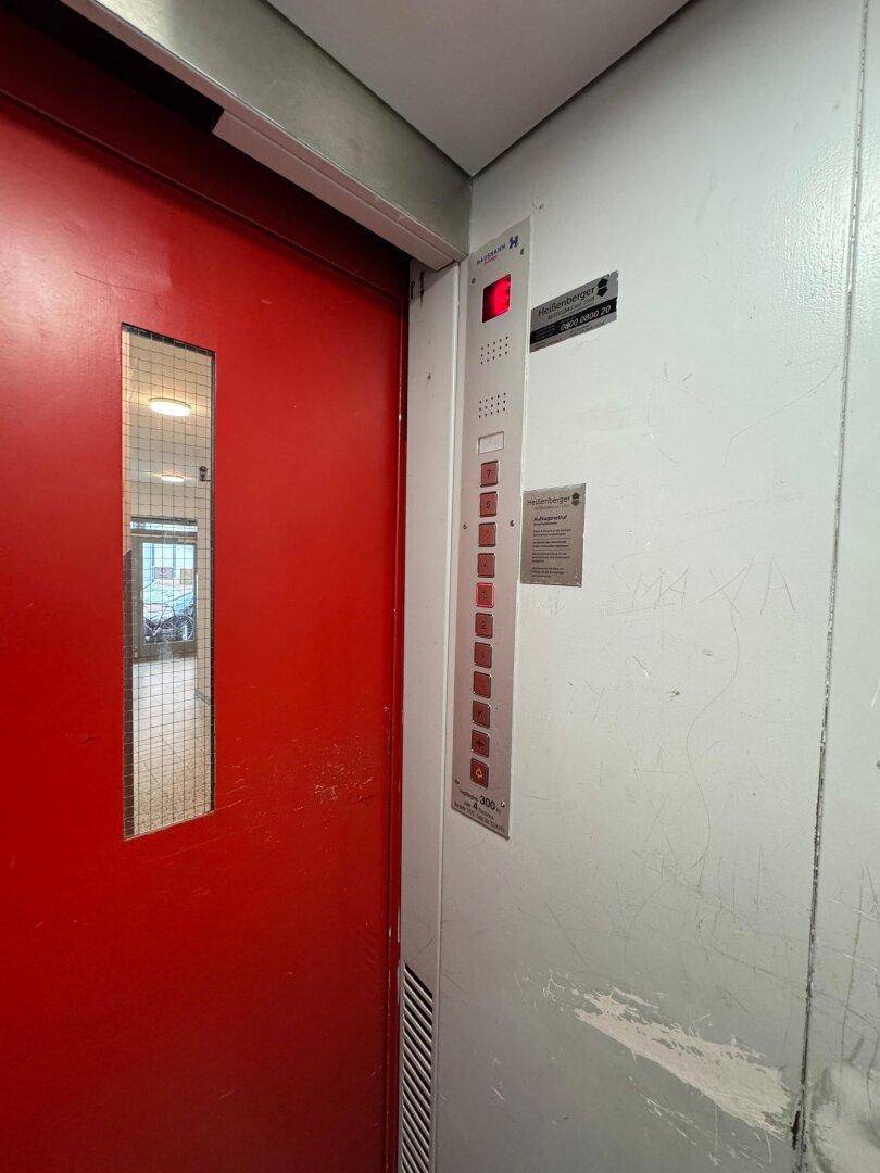 Roter Aufzug im Gebäude mit Bedienfeld und Spuren von Abnutzung.