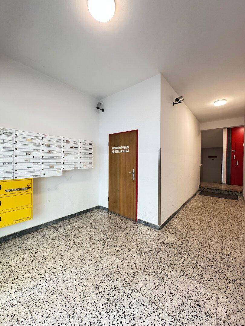 Eingangsbereich des Gebäudes mit Briefkästen, Kinderwagenabstellraum und Überwachungskameras.