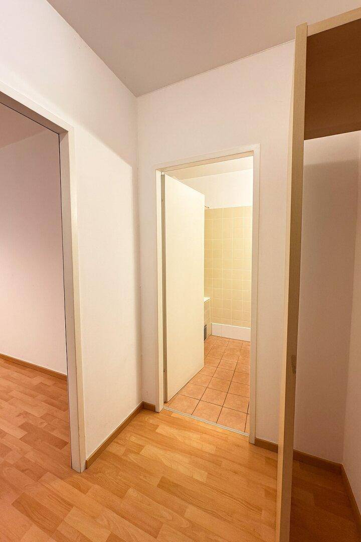 Flur mit Parkettboden und offener Tür zu einem gefliesten Badezimmer.