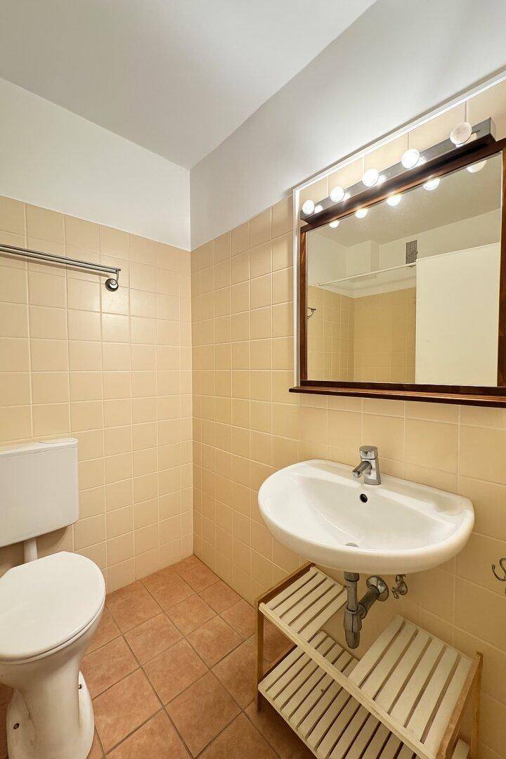 Badezimmer mit beigefarbenen Fliesen, Waschbecken, Toilette und beleuchtetem Spiegel.
