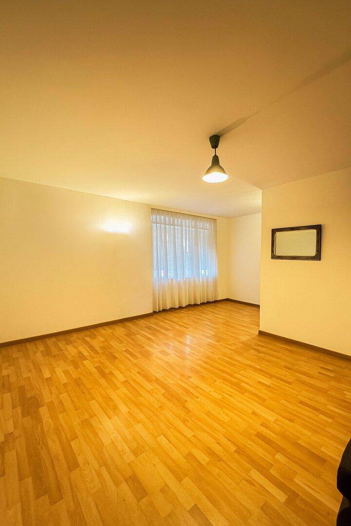 Geräumiges, leeres Zimmer mit Parkettboden, Fenster und einem Wandspiegel.