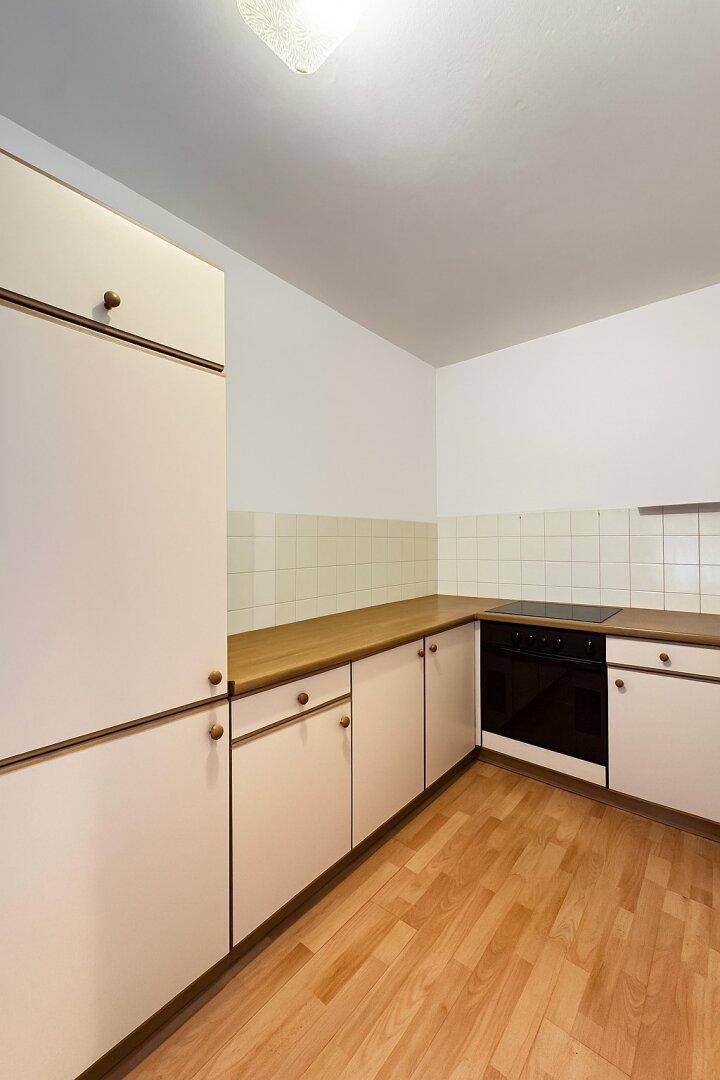 Einfache Einbauküche mit hellen Schränken, Holz-Arbeitsplatte und Herd.