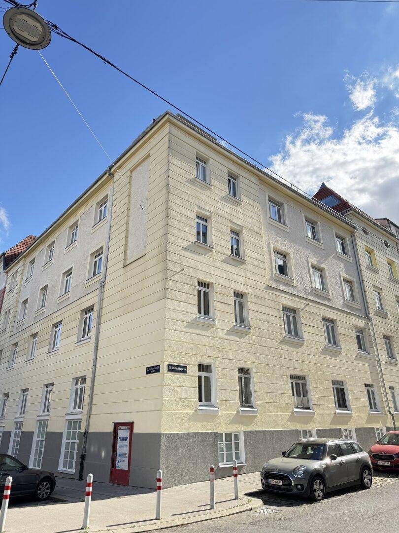 Eckgebäude in der Stadt mit mehreren Etagen und vielen Fenstern, umgeben von parkenden Autos.
