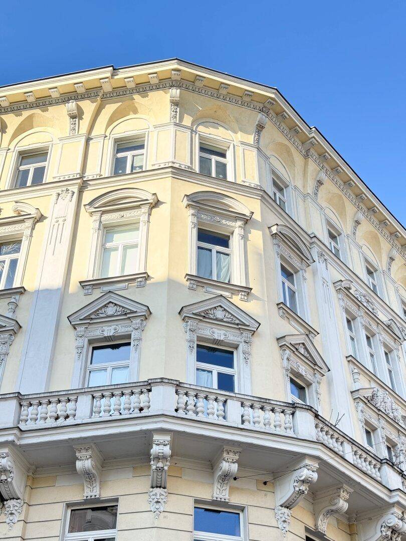 Historisches Eckgebäude mit reich verzierten Fassaden und Balkonen unter strahlend blauem Himmel.