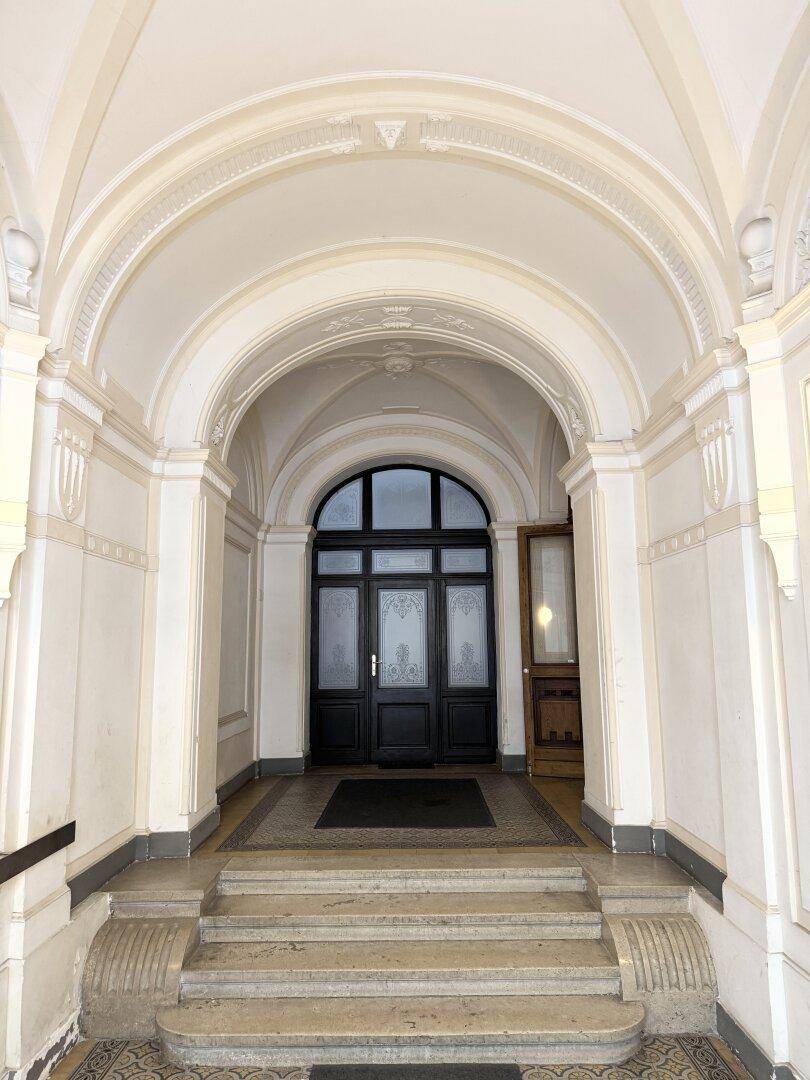 Historischer Gebäudeeingang mit gewölbtem Portal und breiter Steintreppe, die zum Gebäude führt.