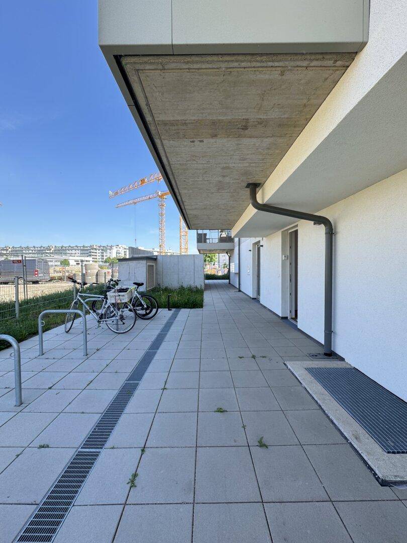 Außenbereich eines Neubaus mit gepflastertem Weg und Fahrradständern.