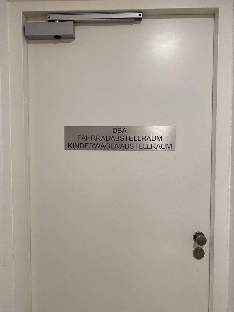 Weiße Tür zu einem Gemeinschaftsraum für Fahrräder und Kinderwagen im Gebäude.