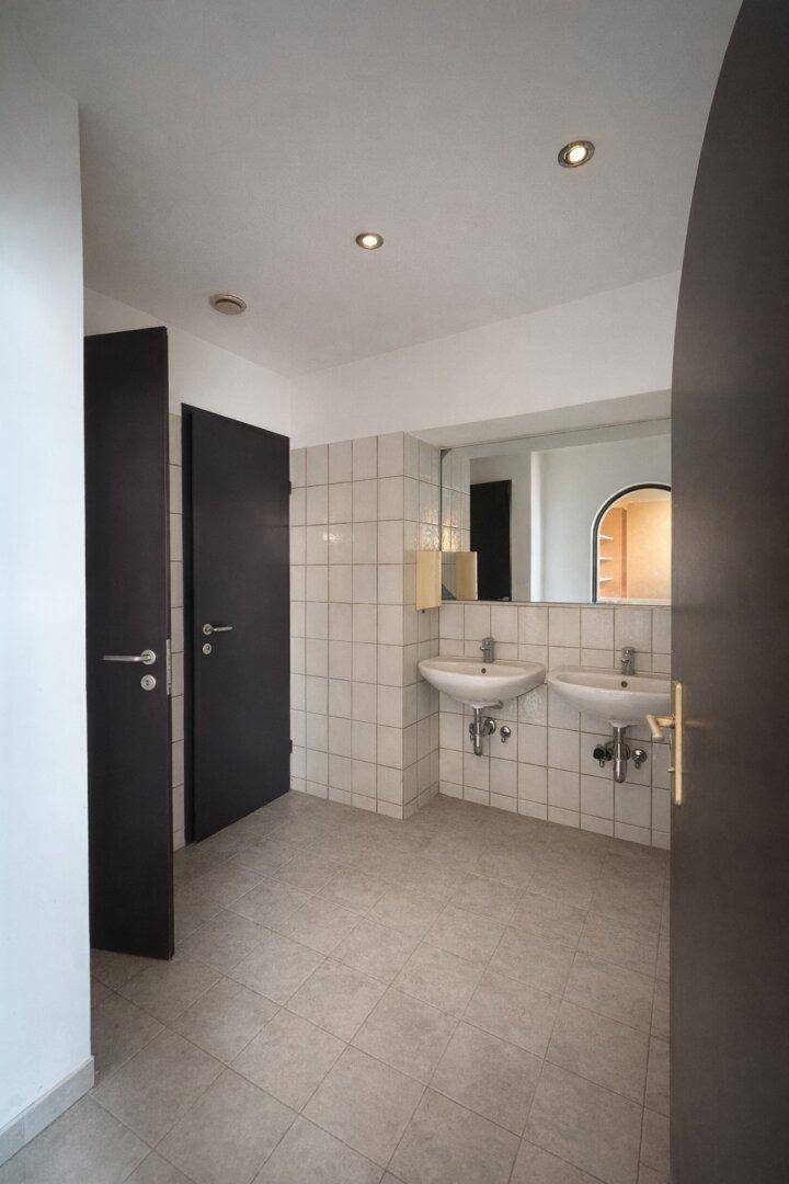 Gewerblicher Waschraum mit zwei Waschbecken, großem Spiegel und Fliesenboden, funktional und sauber.