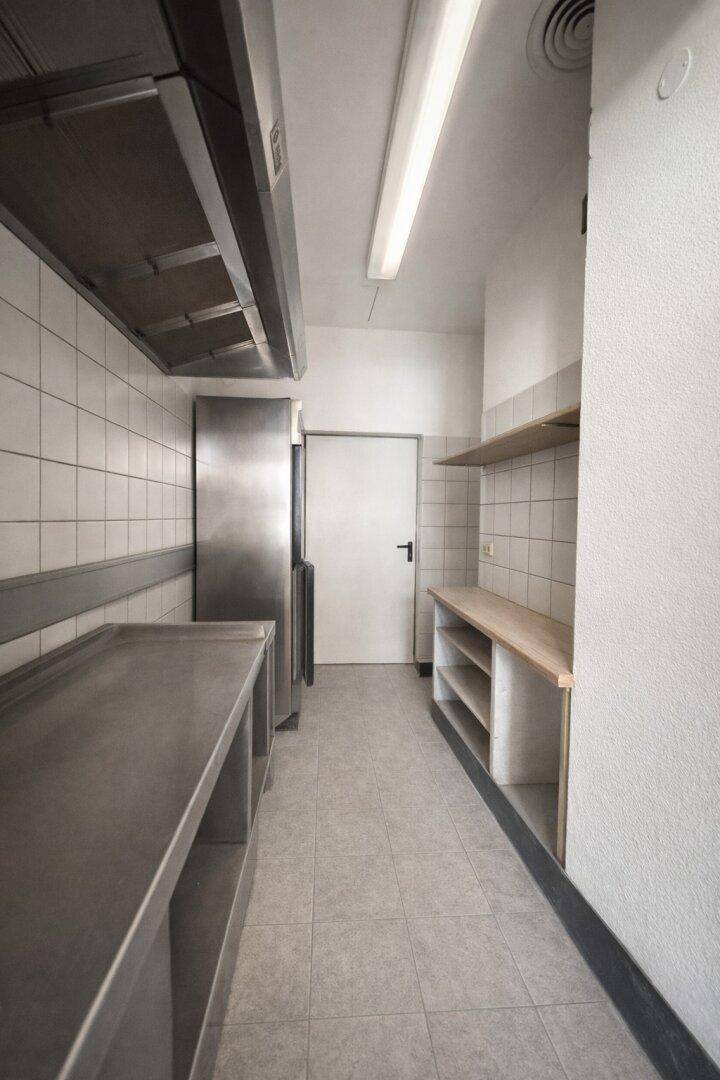 Funktionale Gewerbeküche mit Edelstahlflächen, Fliesenwänden und Abluftsystem, bereit für den Betrieb.