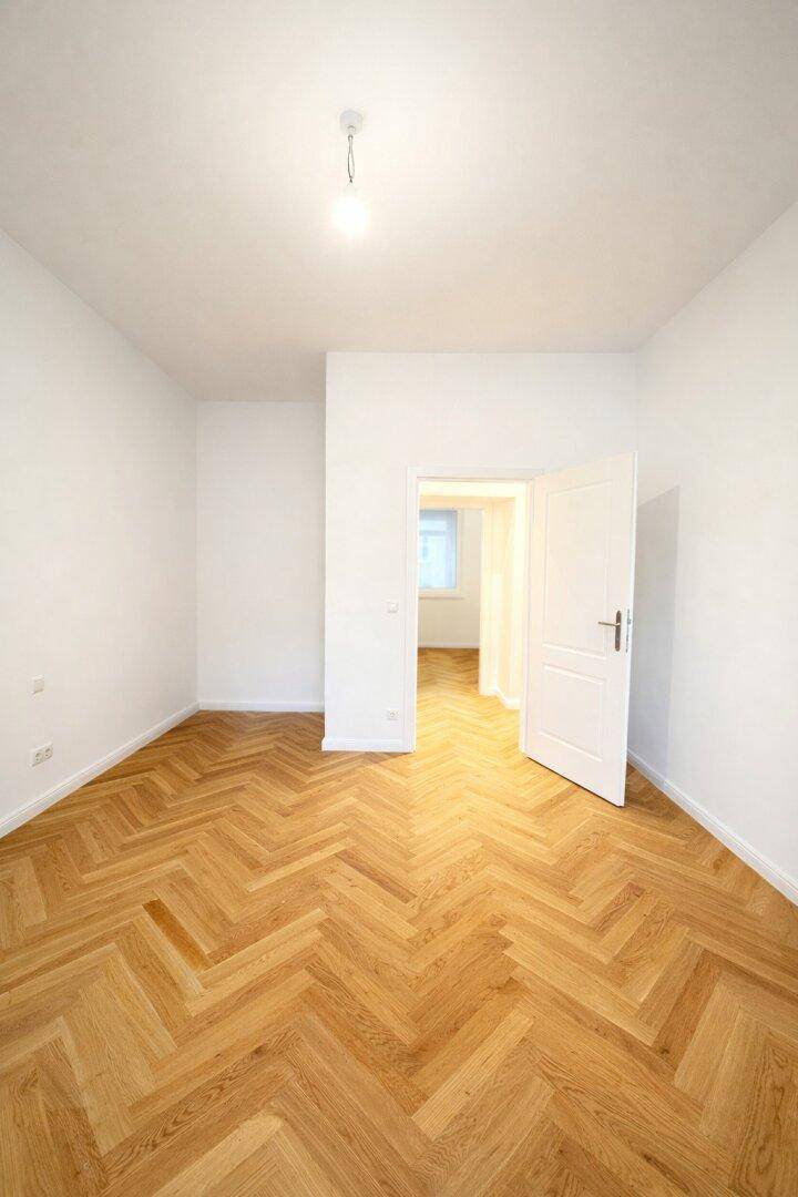 Geräumiges Zimmer mit Fischgrätparkett und weiß gestrichenen Wänden, bereit zur individuellen Gestaltung.