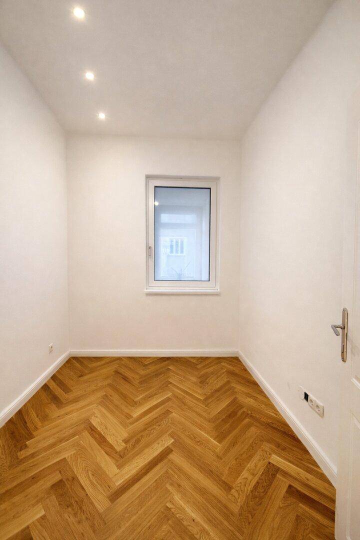 Kleineres Zimmer mit Fischgrätparkett und einem Fenster, ideal als Schlaf- oder Arbeitszimmer.