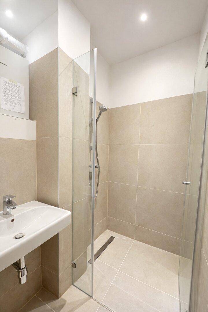 Modernes Badezimmer mit begehbarer Dusche, beigefarbenen Fliesen und minimalistischem Waschbecken.
