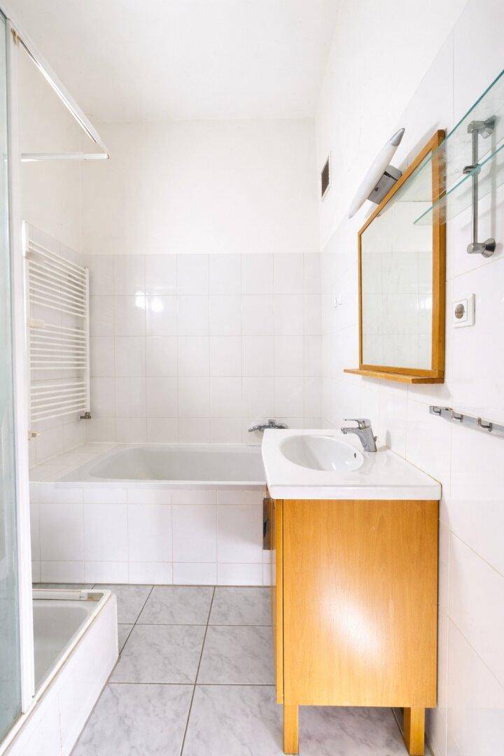 Helles Badezimmer mit Badewanne, Duschkabine und einem Holzwaschtisch mit Spiegel.