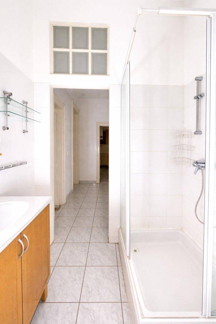 Badezimmer mit Duschkabine und Blick in einen gefliesten Flur, der zu weiteren Räumen führt.