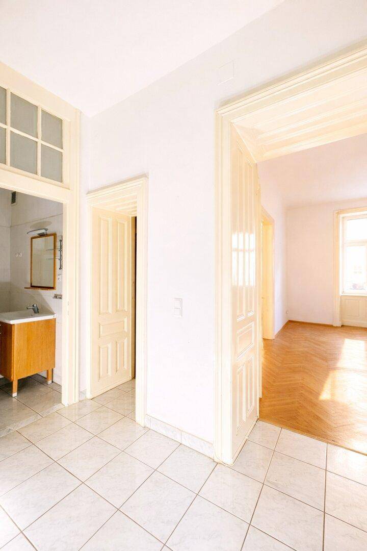 Heller Flur mit Fliesenboden, der zu einem Badezimmer und weiteren Räumen mit Holztüren führt.