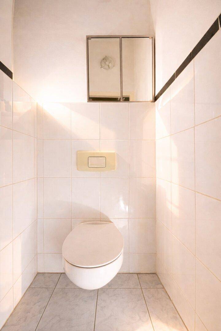 Separates WC mit weißen Fliesen und einer wandmontierten Toilette, hell beleuchtet.