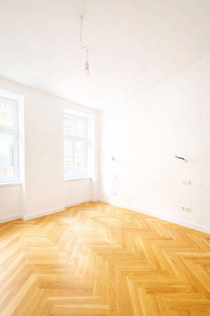 Geräumiges, helles Zimmer mit Fischgrätparkett und weißen Wänden, ideal für individuelle Gestaltung.