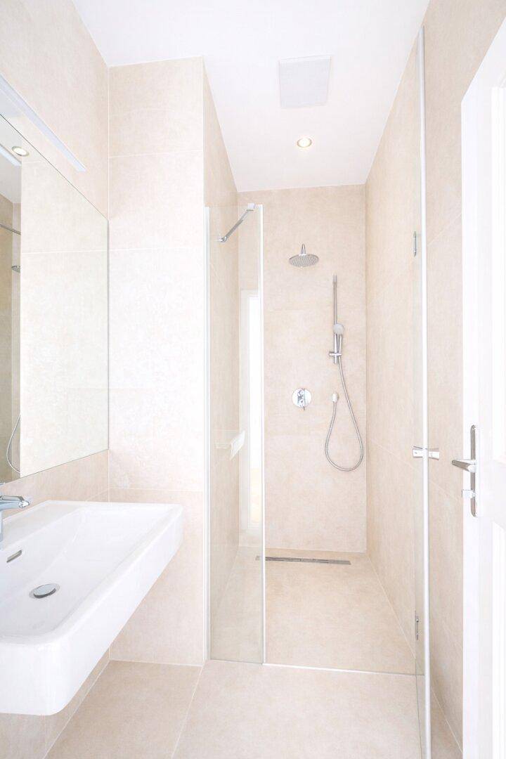 Modernes Badezimmer mit begehbarer Dusche, Wandwaschbecken und hellen Fliesen.