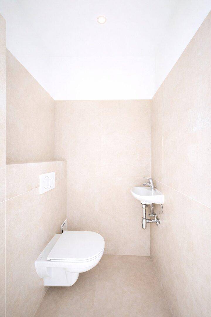 Kompaktes Gäste-WC mit wandhängender Toilette und kleinem Handwaschbecken.