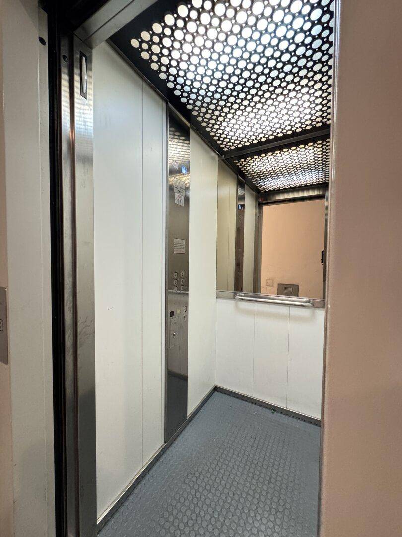 Innenansicht einer modernen Aufzugskabine mit perforierter Decke und Edelstahl.