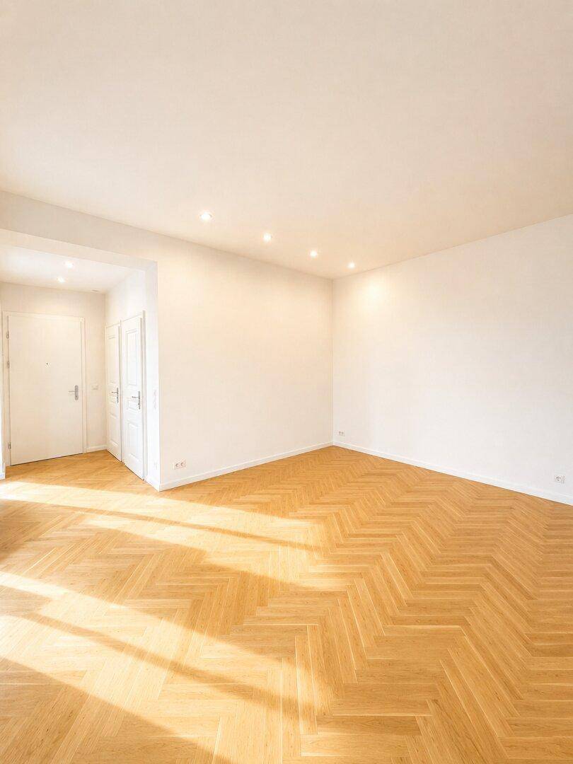 Geräumiges, helles Zimmer mit Fischgrätparkett und Einbaustrahlern in der Decke.