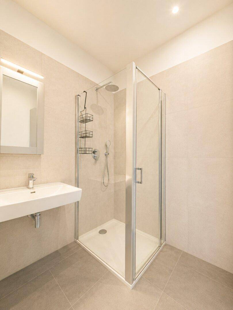 Modernes Badezimmer mit Duschkabine, Waschbecken und hellen Fliesen an Wänden und Boden.