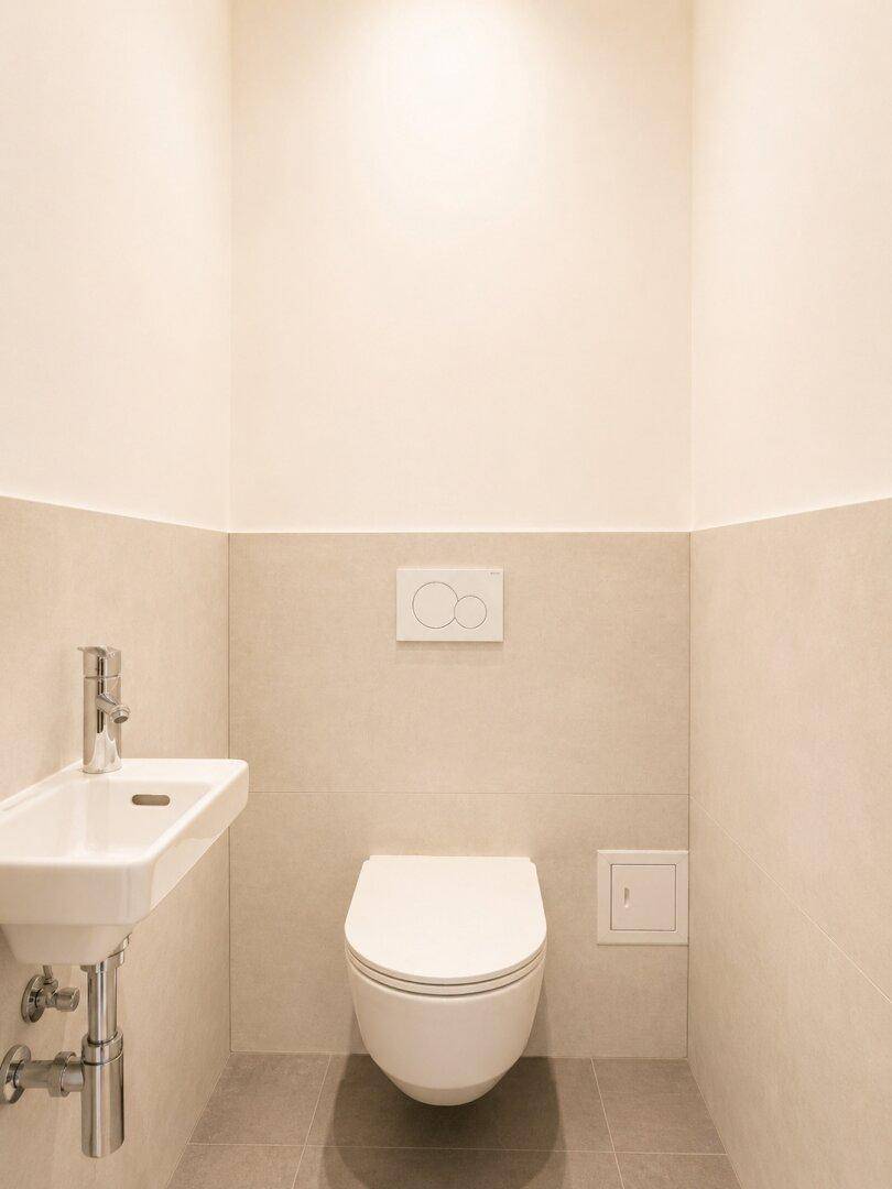 Modernes Gäste-WC mit wandhängendem WC, kleinem Waschbecken und hellen Fliesen.