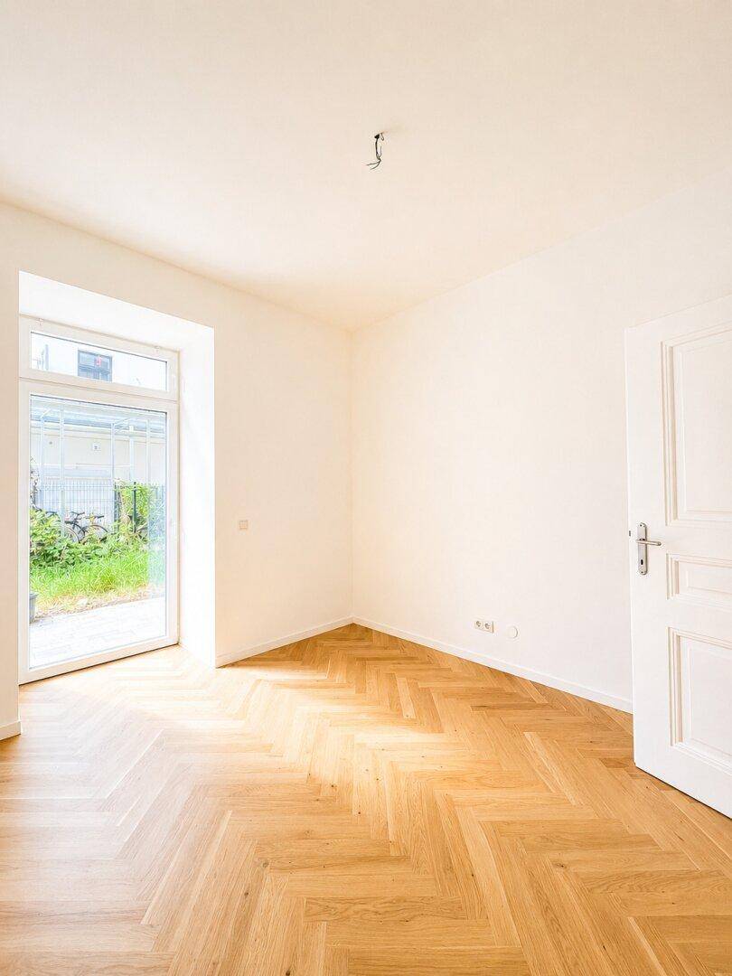 Helles Zimmer mit Fischgrätparkett und großer Fenstertür zum Außenbereich.