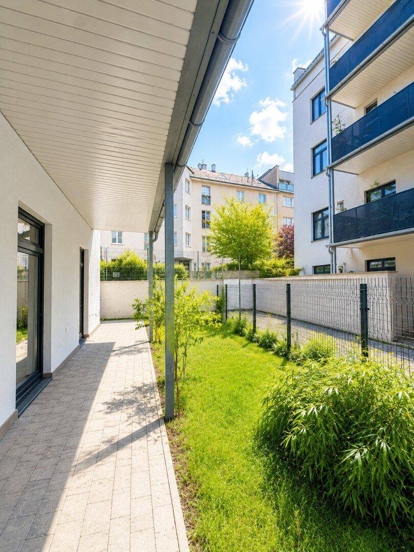 Sonniger Gartenbereich mit gepflastertem Weg und Blick auf das moderne Gebäude.