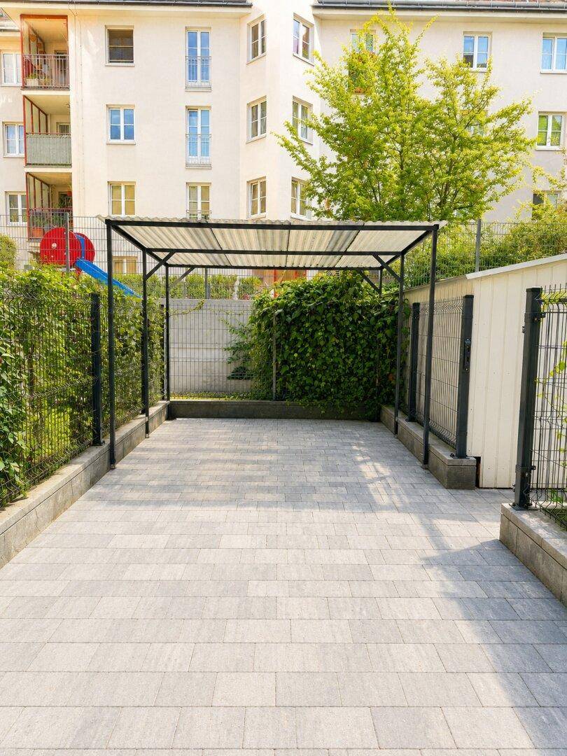Überdachter Parkplatz mit gepflastertem Boden und umzäuntem Bereich.