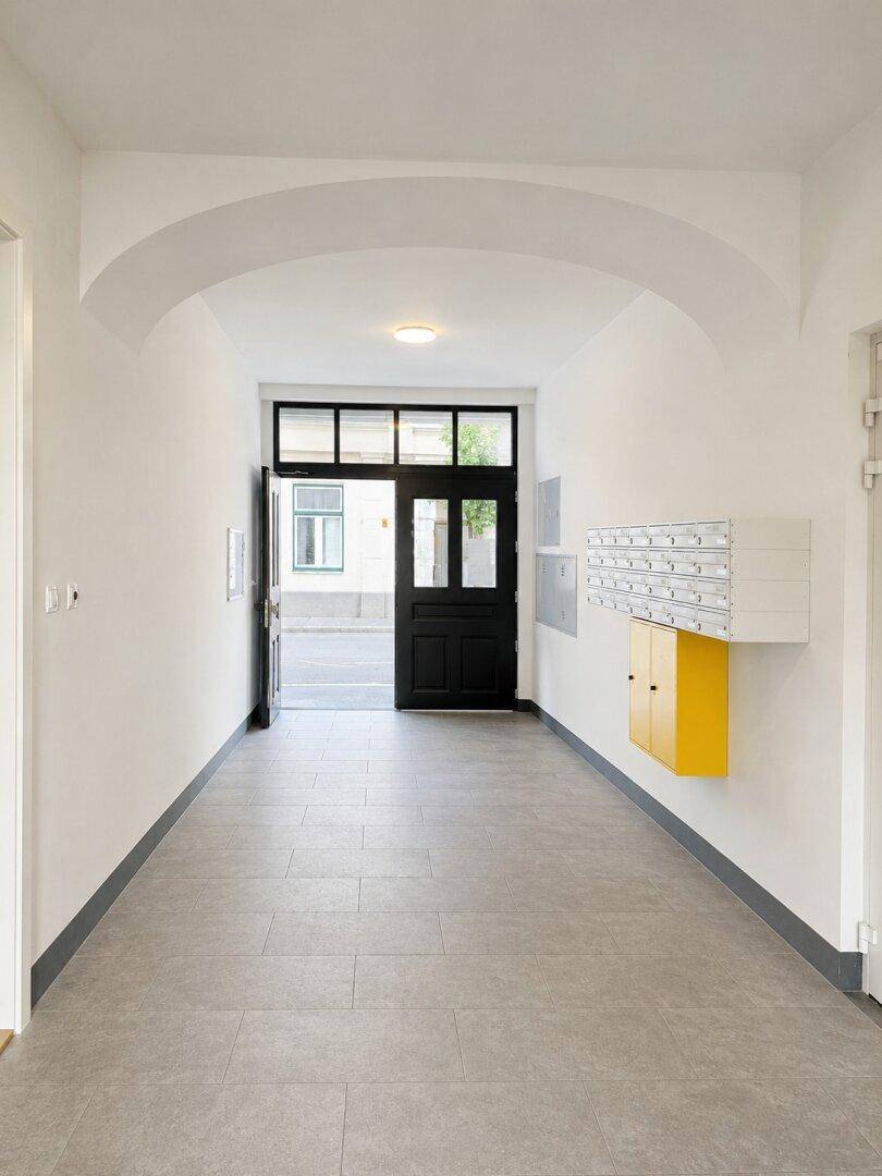 Heller Eingangsbereich des Gebäudes mit Briefkästen und Zugang zur Straße.