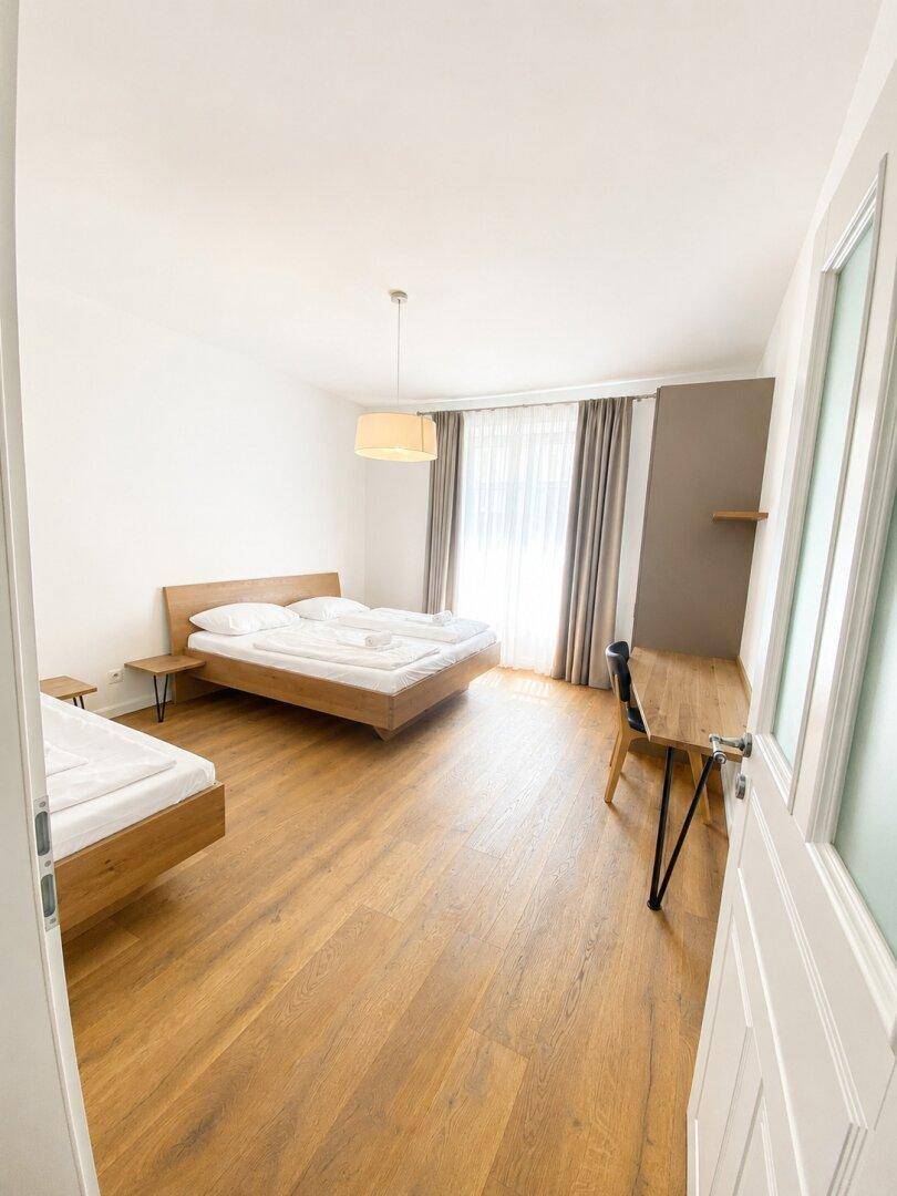 Schlafzimmer mit Holzboden, Doppelbett und Zugang zu einem Balkon, hell und komfortabel.
