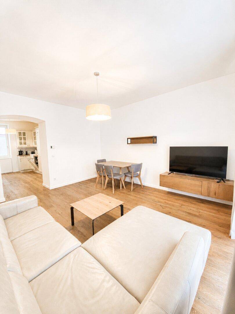 Geräumiger Wohn-Essbereich mit beigem Sofa, Esstisch und Blick in die Küche, offen und einladend.