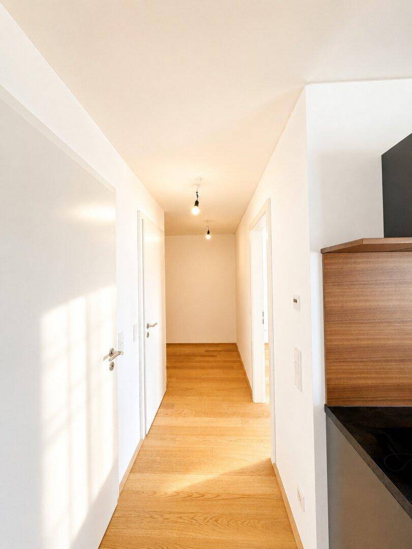 Heller Flur mit Holzboden und weißen Wänden, der zu verschiedenen Räumen führt.