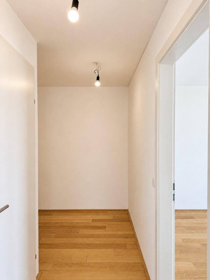 Leerer, heller Eingangsbereich mit Holzboden und weißen Wänden, der einen klaren Übergang bietet.