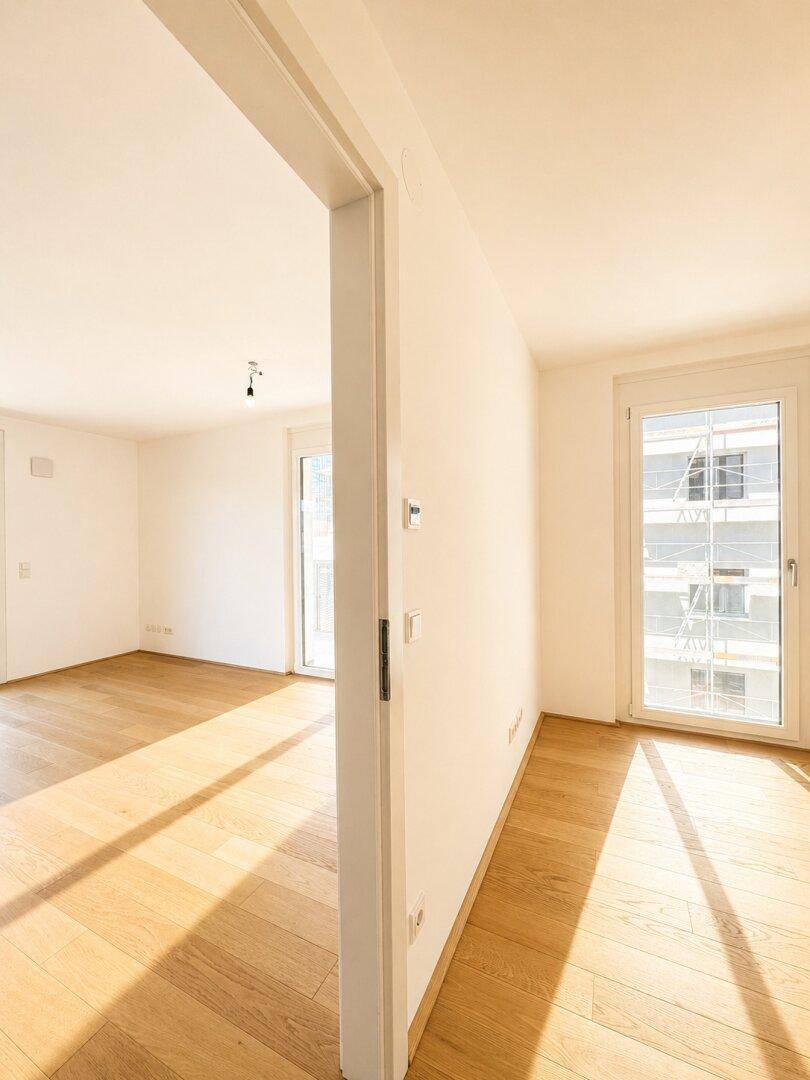 Geräumiges, helles Wohnzimmer mit Holzboden und Zugang zu einem Balkon durch eine Fenstertür.
