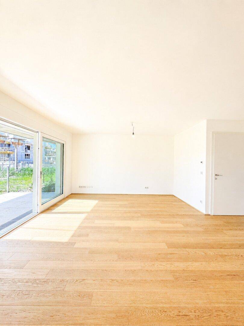 Geräumiges, helles Wohnzimmer mit Parkettboden und großen Fenstern, die viel Licht hereinlassen.