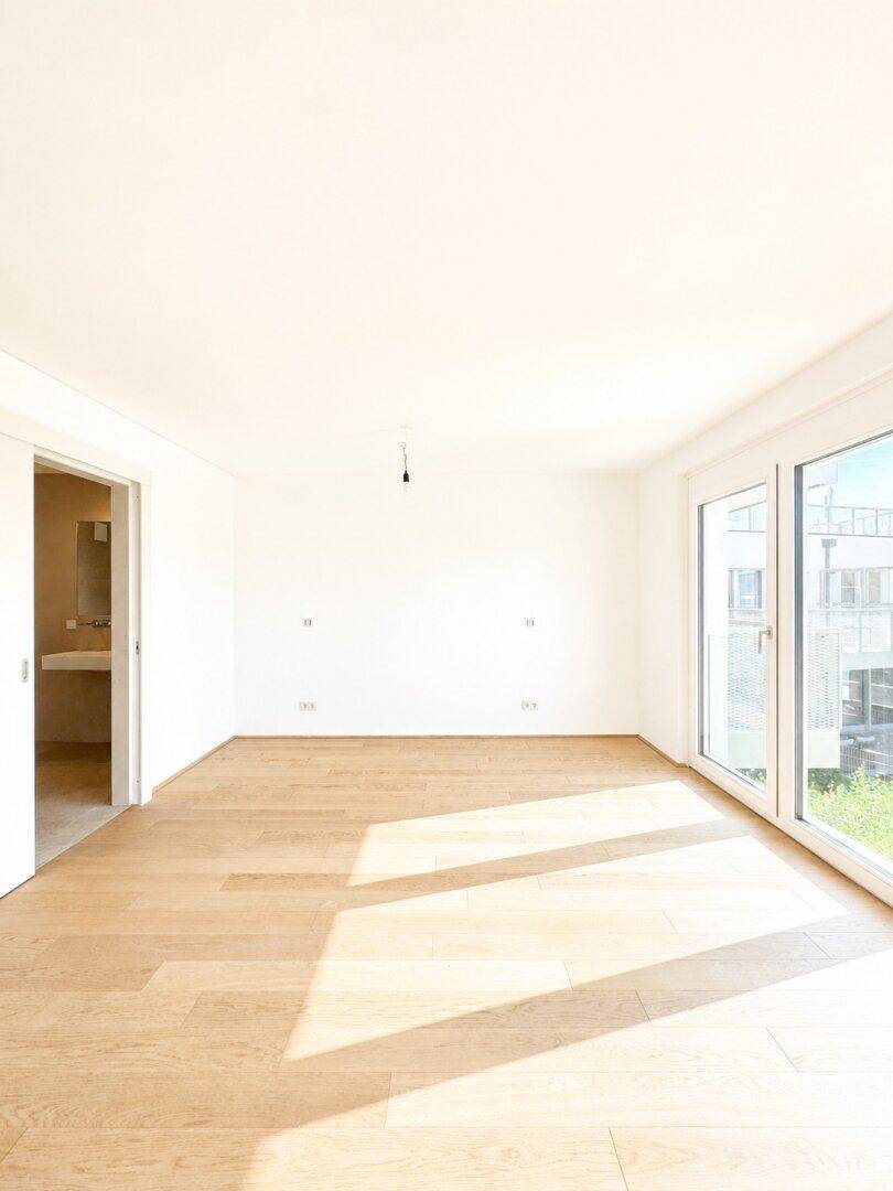 Lichtdurchfluteter Raum mit Holzboden und großen Fenstern, die einen Blick nach draußen bieten.