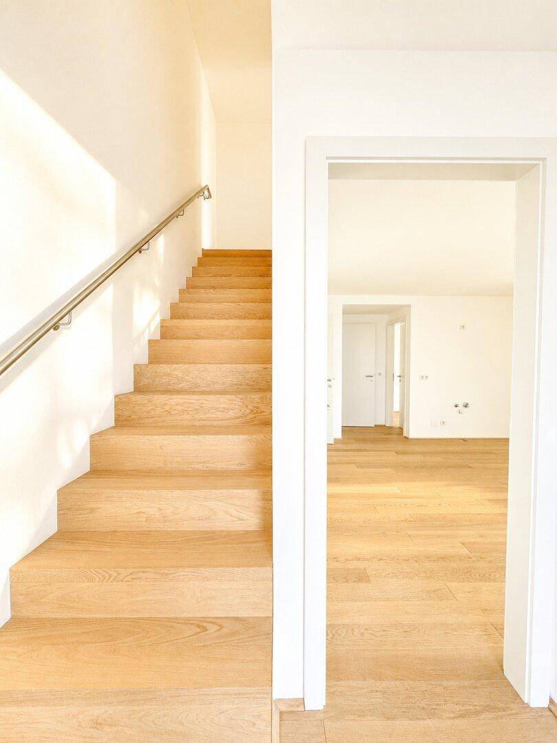 Heller Flur mit Holztreppe und Parkettboden, der zu weiteren Räumen führt.