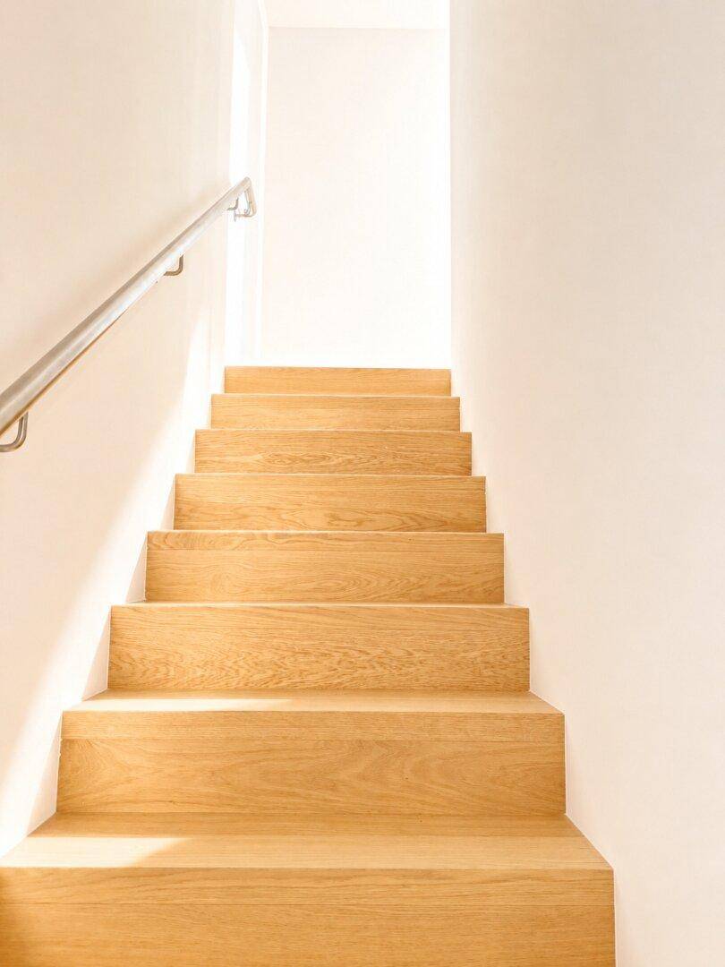Moderne Holztreppe mit Edelstahlgeländer, die in ein helles Obergeschoss führt.