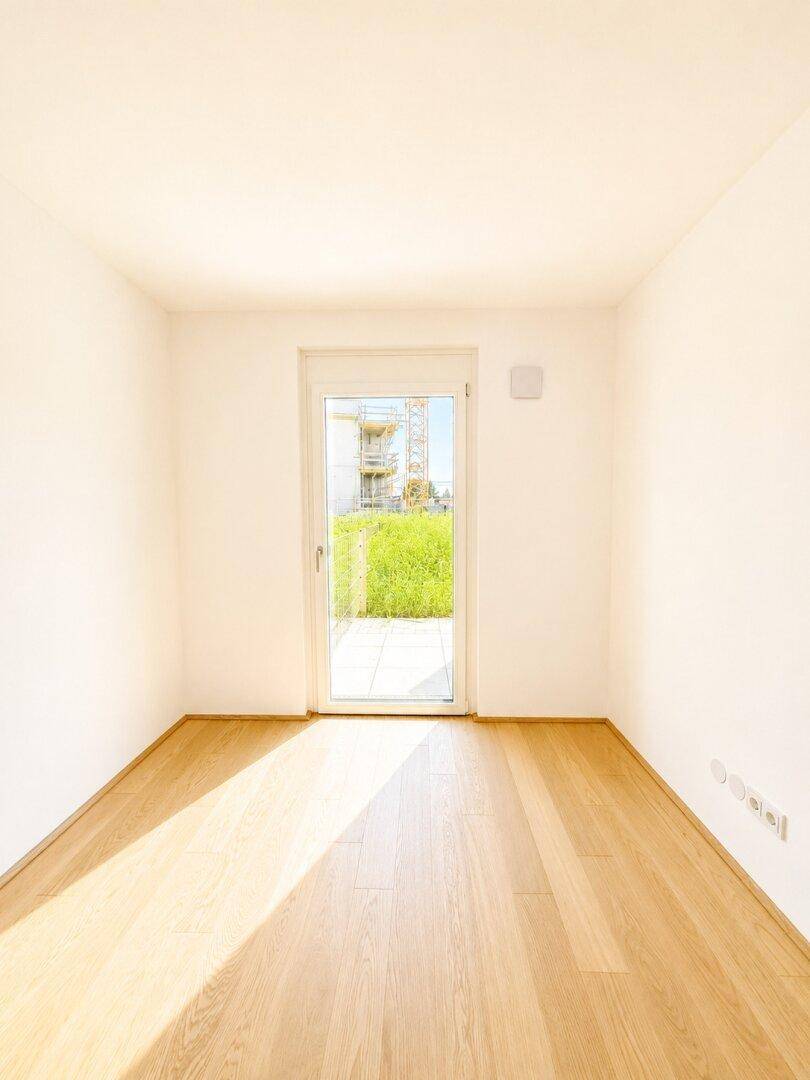 Helles Zimmer mit Parkettboden und Zugang zu einer Terrasse oder einem kleinen Gartenbereich.