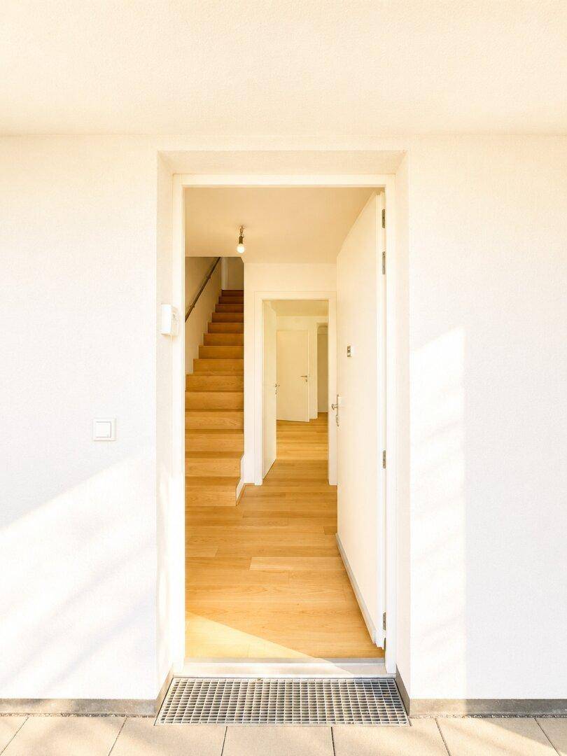Eingangsbereich mit heller Tür und Blick auf eine Holztreppe und weitere Räume.