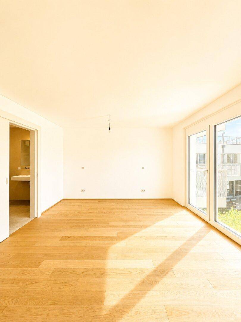 Lichtdurchfluteter Raum mit Holzboden und großen Fenstern, die einen Blick nach draußen bieten.