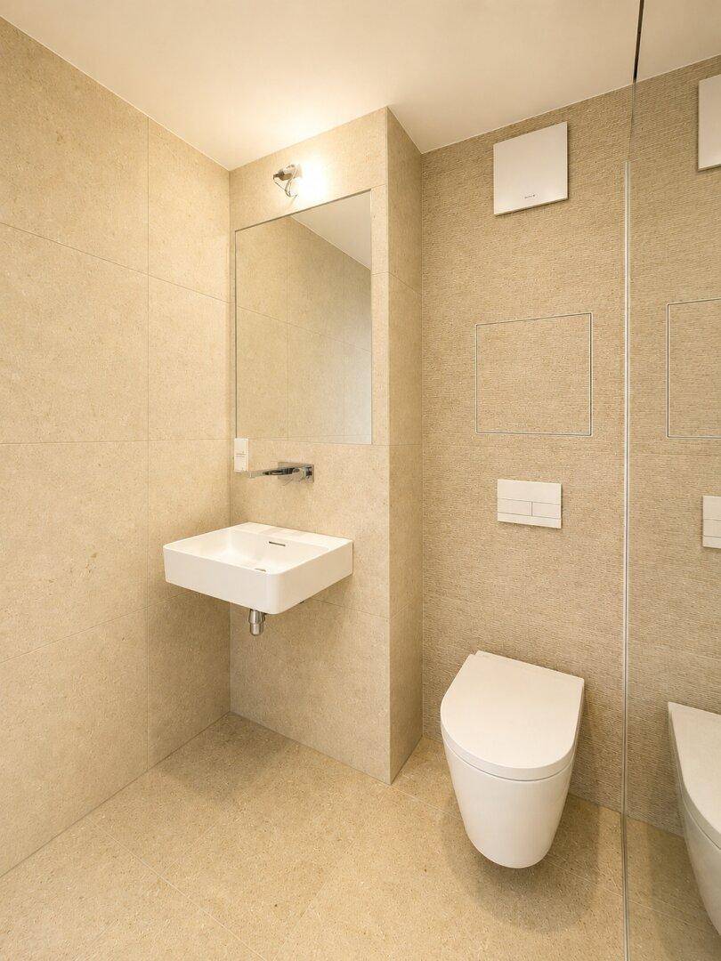 Kleines, modernes Gäste-WC mit beigefarbenen Fliesen, wandhängender Toilette und Waschbecken.