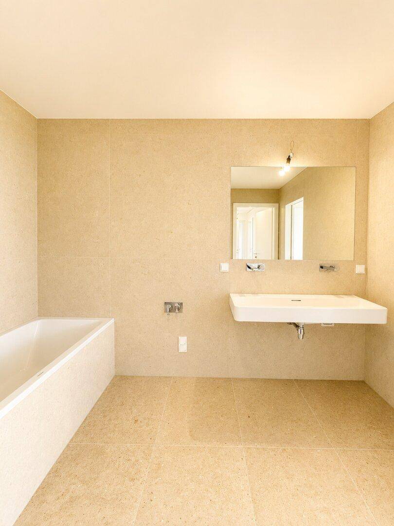 Modernes Badezimmer mit beigefarbenen Fliesen, Badewanne und großem Waschbecken mit Spiegel.